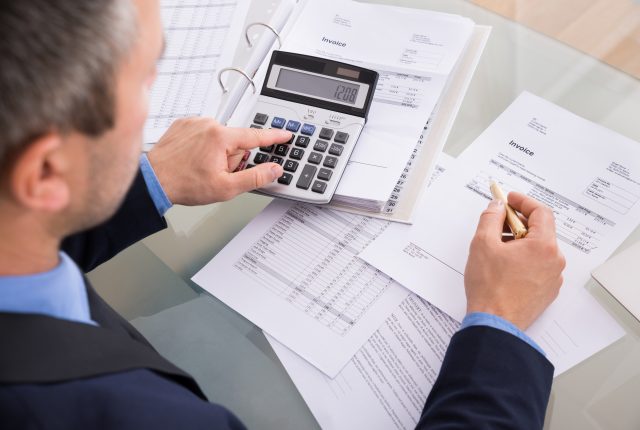businessman using a calculator and reviewing financial documents at a desk