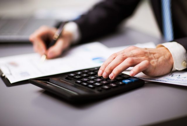 Person using a calculator while writing on financial documents at a desk in a professional setting.