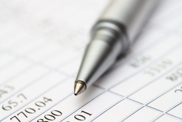 Close-up of a silver pen resting on a financial spreadsheet with numerical data in rows and columns.