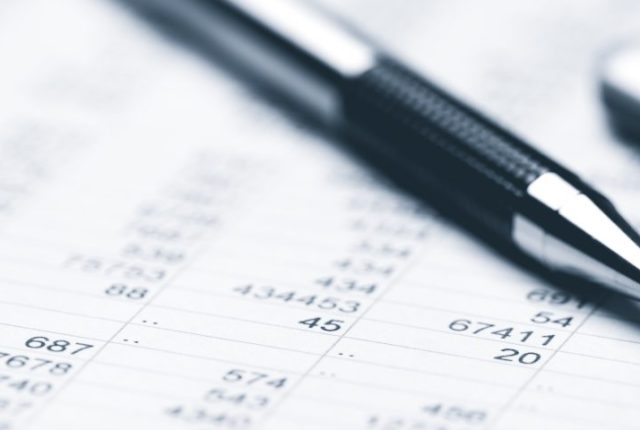 close up of a pen and calculator resting on financial spreadsheets filled with numerical data